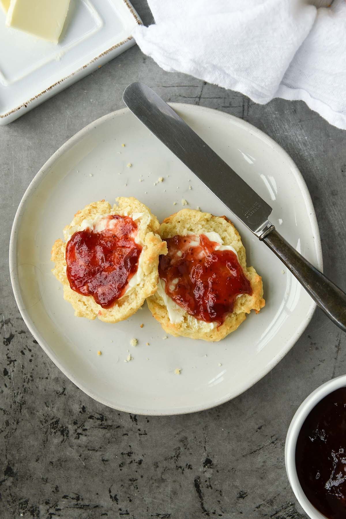 Above view of a buttered and jellied biscuit with a small bowl of jelly and some butter.
