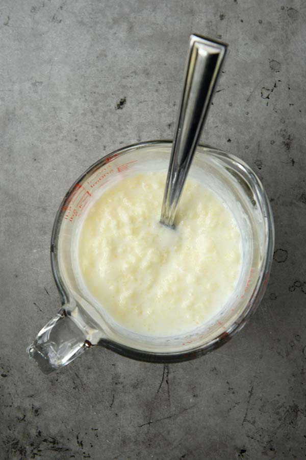 A liquid measuring cup with the melted butter being stirred into the very cold buttermilk.