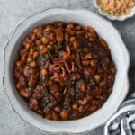 Above view of a serving bowl of bbq baked beans, a striped towel, and a small dish of brown sugar.