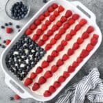 Above view of the North American flag cake with a striped towel and two bowls of raspberries and blueberries on the side.