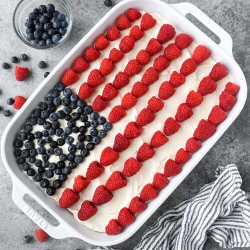 Above view of the North American flag cake with a striped towel and two bowls of raspberries and blueberries on the side.