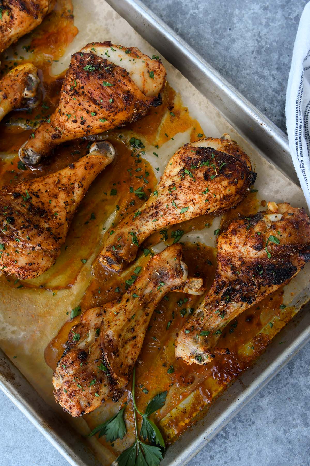 Above view of chicken drumsticks on a baking sheet with a striped towel.