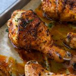 Two chicken legs on a baking sheet surrounded by other chicken drumsticks.