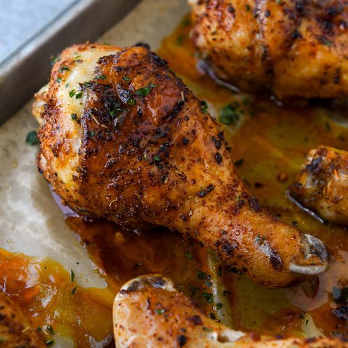 Two chicken legs on a baking sheet surrounded by other chicken drumsticks.