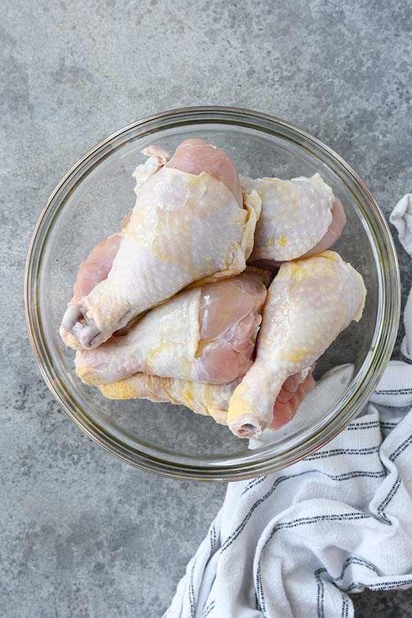 Step two is a bowl with chicken legs with a drizzle of oil.