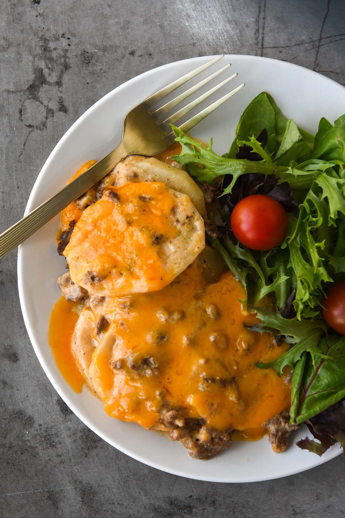 Above view of a plateful of ground beef casserole, a side salad, and a gold fork. 