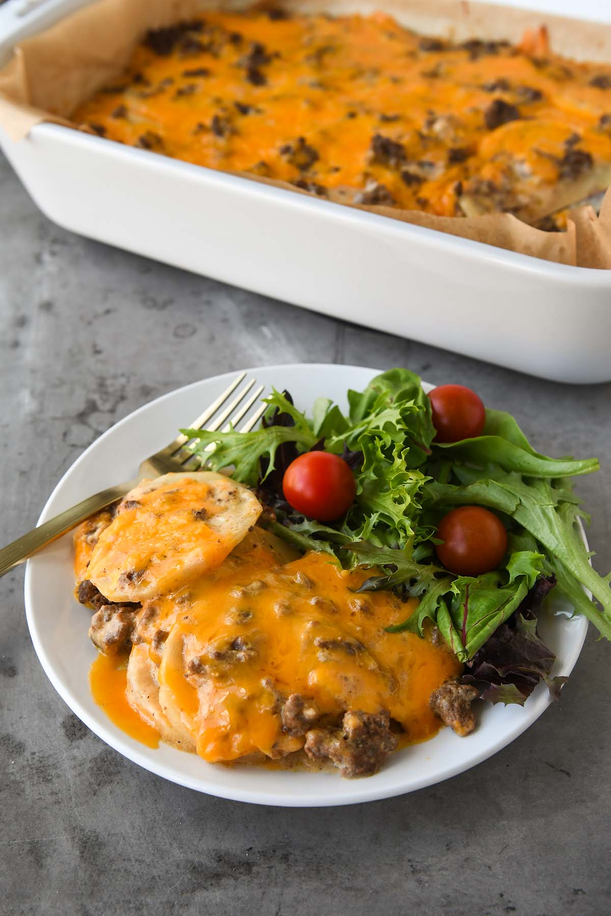 A plateful of ground beef casserole, a side salad, and a fork. The casserole dish is in the background.