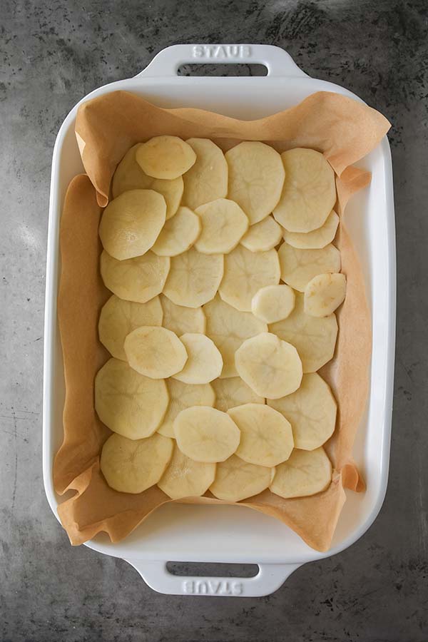 Step four is a casserole dish with a layer of thinly sliced potatoes added to the bottom.