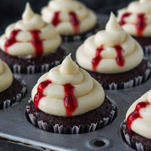 A metal cupcake tray filled with decorated vampire bite cupcakes.