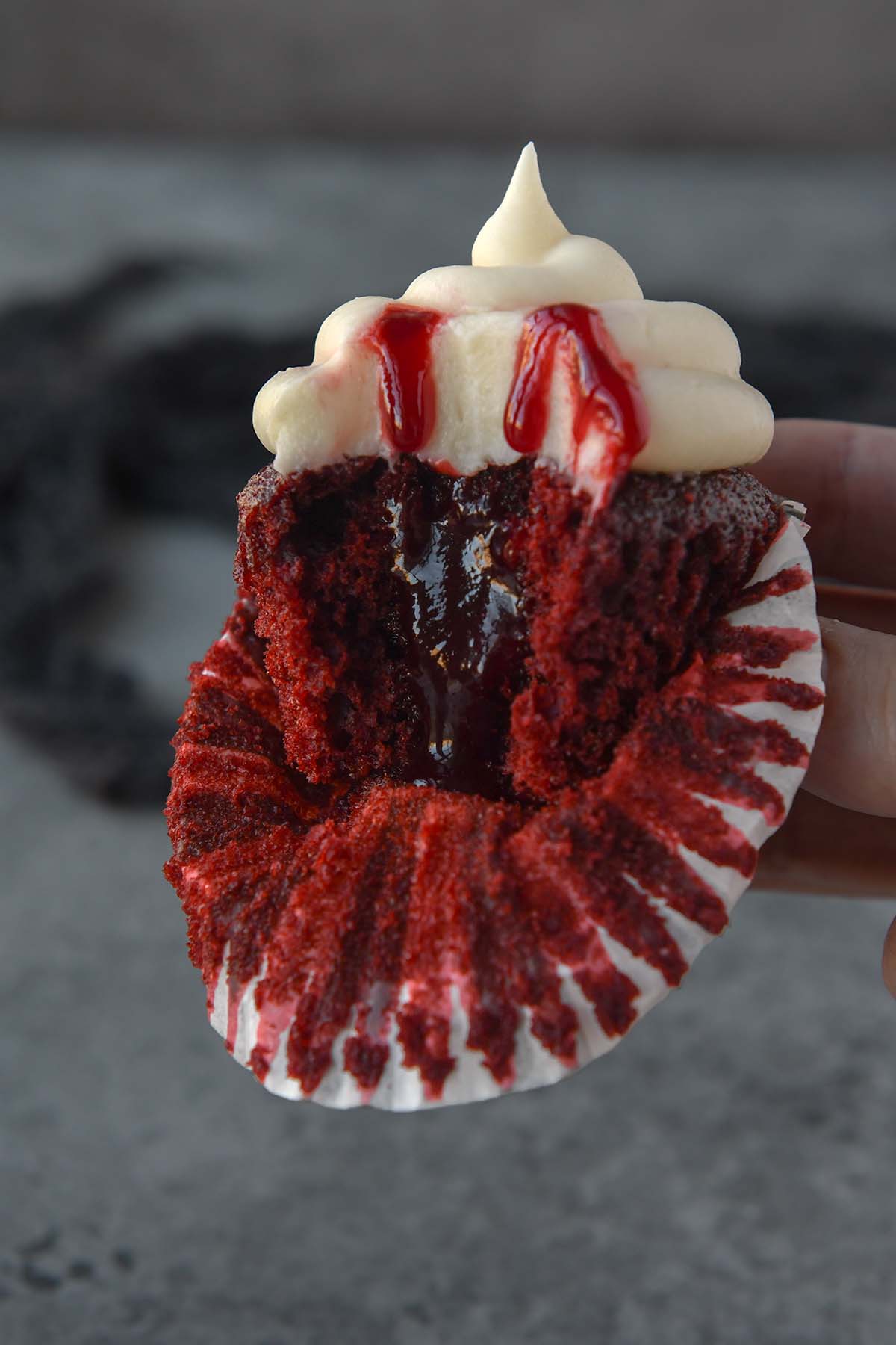 Up close of a cupcake with a bite missing to show the jam filled center. Raspberry jam drips down from the frosting and the cupcake wrapper is folded down.