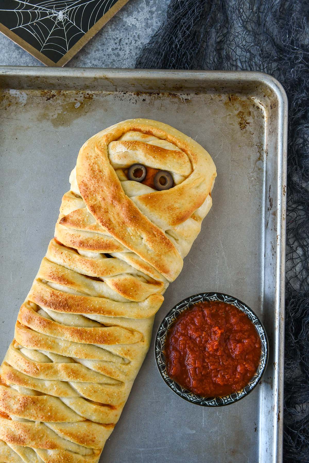 Above view of the pizza mummy on a baking sheet with a side of sauce.
