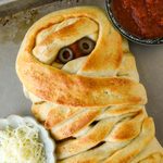 Above view of the pizza mummy with a side of sauce and a small bowl of cheese.
