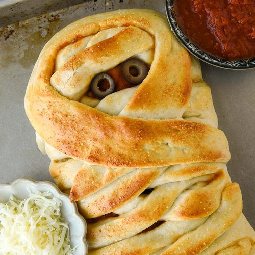 Above view of the pizza mummy with a side of sauce and a small bowl of cheese.