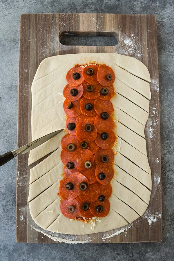 Step four is the pepperoni and olives getting added on top of the cheese. Then the dough gets sliced up the sides.