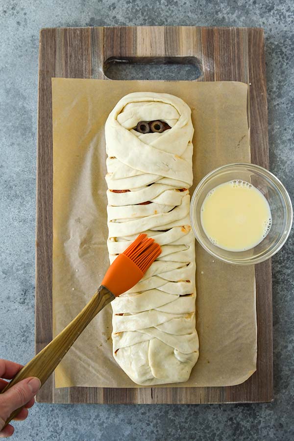 Step six is adding the olive eyes, spreading the egg wash over the dough and sprinkling on the garlic salt.