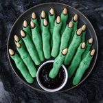 Above view of a dark plate of witch finger cookies with a small bowl of raspberry jam.