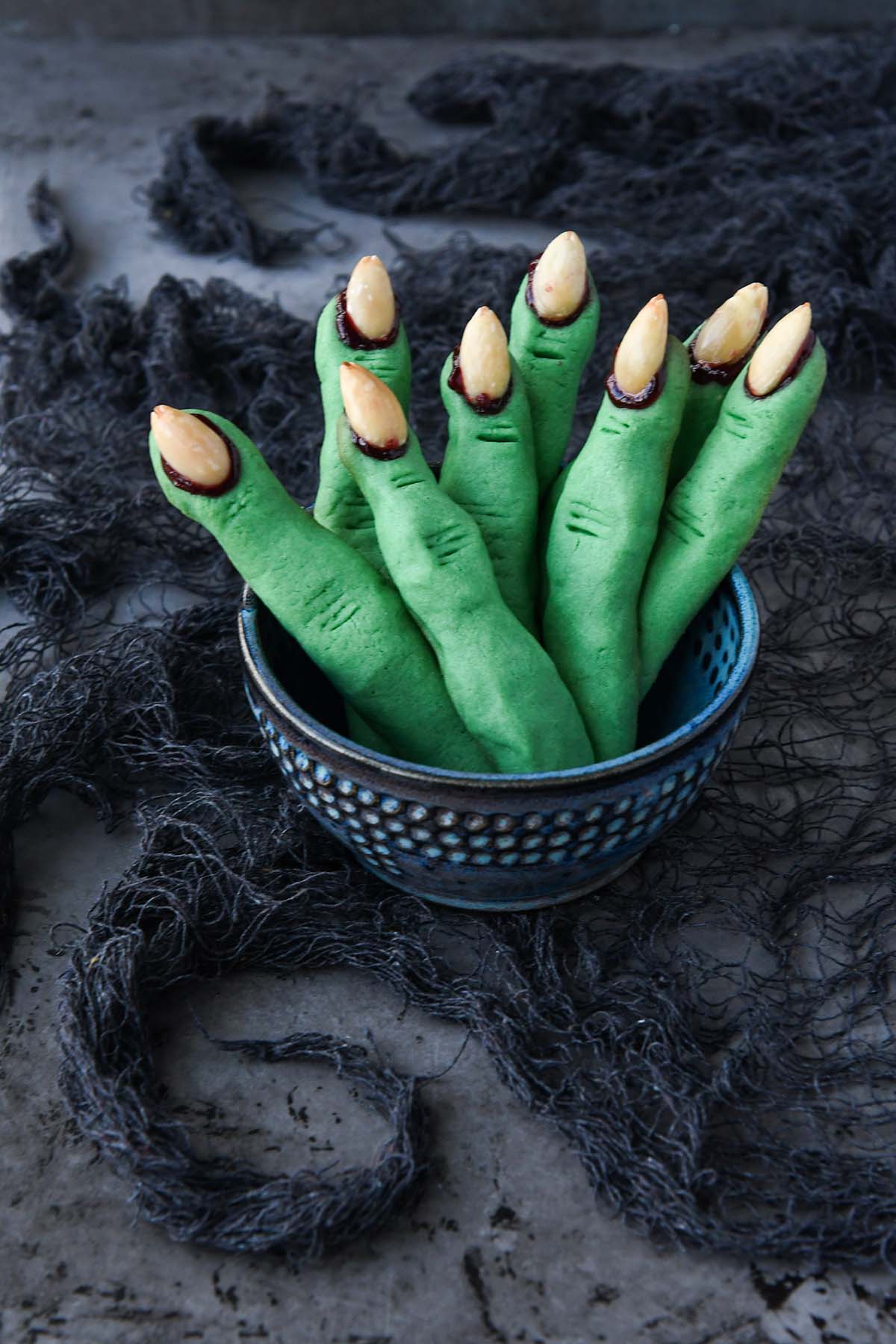 A blue bowl of witch finger cookies on a grey stringy fabric